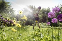 Vista attraverso i fiori di donna matura in giardino irrigazione fiori con hosepipe — Foto stock