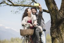 Young couple taking selfie on bicycle in rural landscape — Stock Photo