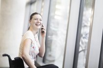 Junge Frau im Rollstuhl vor Eingangstür telefoniert mit Smartphone — Stockfoto