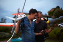 Zwei männliche Freunde halten ferngesteuerte Flugzeuge in der Hand und schauen auf das Smartphone — Stockfoto