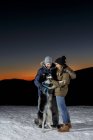 Пара игр с собакой в снегу ночью — стоковое фото