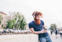 Young male hipster with red hair and beard choosing headphone music in city — Stock Photo