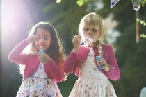 Two cute girls blowing bubbles in garden — Stock Photo