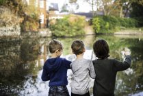 Three young boys, standing beside lake, rear view — Stock Photo