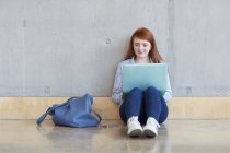 Молода студентка сидить на підлозі, використовуючи ноутбук у коледжі вищої освіти — стокове фото