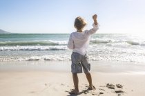 Visão traseira de comprimento total do menino na praia jogando pedras no oceano — Fotografia de Stock