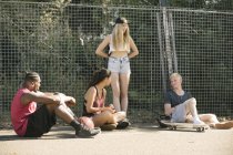 Four adult skateboarder friends sitting chatting on basketball court — Stock Photo