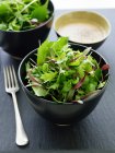Bowl of mixed greens salad and fork on table — Stock Photo