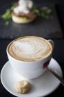 Xícara de cappuccino com biscoito e colher na mesa — Fotografia de Stock