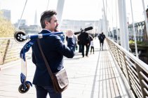 Businessman carrying scooter, Hungerford Bridge, London, UK — Stock Photo
