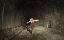Menina no túnel ferroviário deserto, caminhando ao longo da trilha, visão traseira — Fotografia de Stock