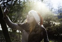 Молодая женщина носит на улице рождественскую шляпу, делает селфи со смартфоном — стоковое фото