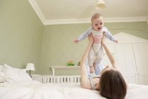 Women lying on bed holding up baby daughter — Stock Photo
