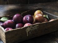 Primer plano de fruta orgánica fresca, ciruelas y manzanas en caja - foto de stock