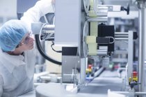 Trabajador operando maquinaria en línea de producción en planta farmacéutica - foto de stock