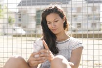 Frau liest Smartphone-Updates am Maschendrahtzaun — Stockfoto