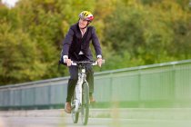 Uomo d'affari in giacca e cravatta in bicicletta sul ponte, attenzione selettiva — Foto stock