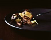 Profiteroles cubiertos de chocolate y cuchara de ratón de chocolate en el plato - foto de stock