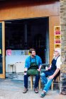 Senior Handwerker trinkt Kaffee und plaudert mit jungem Mann vor Werkstatt — Stockfoto