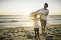 Padre e hijo de pie en la playa, sosteniendo tabla de surf - foto de stock