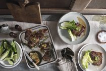 Порции стейков с листьями салата, поднос для выпечки с вареным мясом, миска свежих овощей на столе, натюрморт — стоковое фото