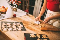 Abgeschnittenes Bild einer Frau, die Weihnachtskekse mit Ausstecher an der Küchentheke schneidet — Stockfoto