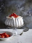Morango coberto pavlova em suporte de bolo de vidro com servidor de bolo e tigela de morangos — Fotografia de Stock