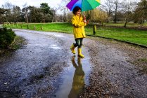 Niño en anorak amarillo llevando paraguas en el parque - foto de stock