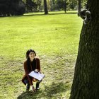 Молода жінка присікає в парку, дивлячись на білку на дереві — стокове фото