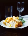 Pesce impanato con patatine fritte, rucola e fetta di limone su piatto bianco — Foto stock