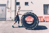 Young male cross trainer pushing large tyre outside gym — Stock Photo
