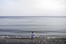 Rear view of small boy crouching and playing at Lake Ontario, Oshawa, Canada — Stock Photo