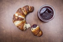 Broken croissant on wooden table with jam — Stock Photo