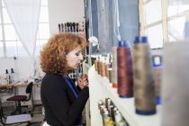 Mujer en taller de costura seleccionando hilo de estante - foto de stock