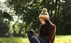Молодая женщина сидит на траве в парке, учится — стоковое фото