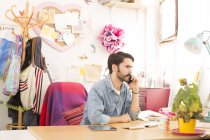Junge männliche Designerin spricht in Druckereistudio mit Smartphone — Stockfoto