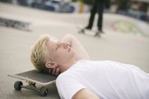 Молодий чоловік скейтбордист лежить в скейтпарку з закритими очима — стокове фото