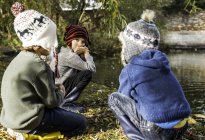 Троє молодих хлопчиків, на відкритому повітрі, присідають біля озера — стокове фото