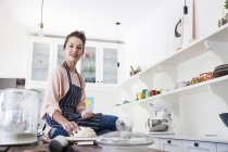 Портрет молодої жінки, що сидить на кухонній лічильниці, готує тісто — стокове фото