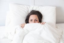 Woman hiding under covers in bed — Stock Photo