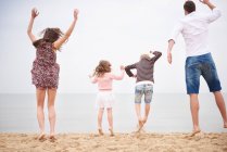 Famiglia saltando sulla spiaggia contro il cielo insieme — Foto stock