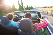 Vista traseira do casal dirigindo conversível na estrada rural iluminada pelo sol, Maiorca, Espanha — Fotografia de Stock