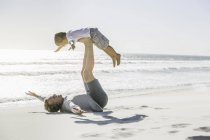 Padre acostado en la playa levantando hijo - foto de stock