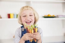 Retrato de menina bonito na cozinha segurando monte de cenouras coloridas — Fotografia de Stock