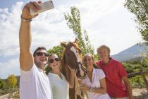 Novio y amigos tomando selfie smartphone con caballo en establos rurales - foto de stock