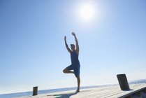 Man on pier standing on one leg arms raised exercising — Stock Photo