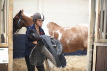 Молодая женщина снимает седло с лошади — стоковое фото