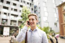 Joven hombre de negocios hablando en el teléfono inteligente fuera de la oficina de la ciudad, Londres, Reino Unido - foto de stock