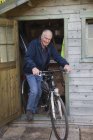 Senior homem de bicicleta por galpão — Fotografia de Stock