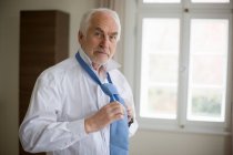 Portrait of old man putting on tie — Stock Photo